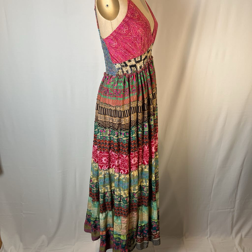 A sleeveless maxi dress displayed on a mannequin against a white fabric backdrop. The dress features a bright pink patterned bodice and a long, flowing skirt with a multicolor geometric and floral pattern in pink, green, blue, and beige.