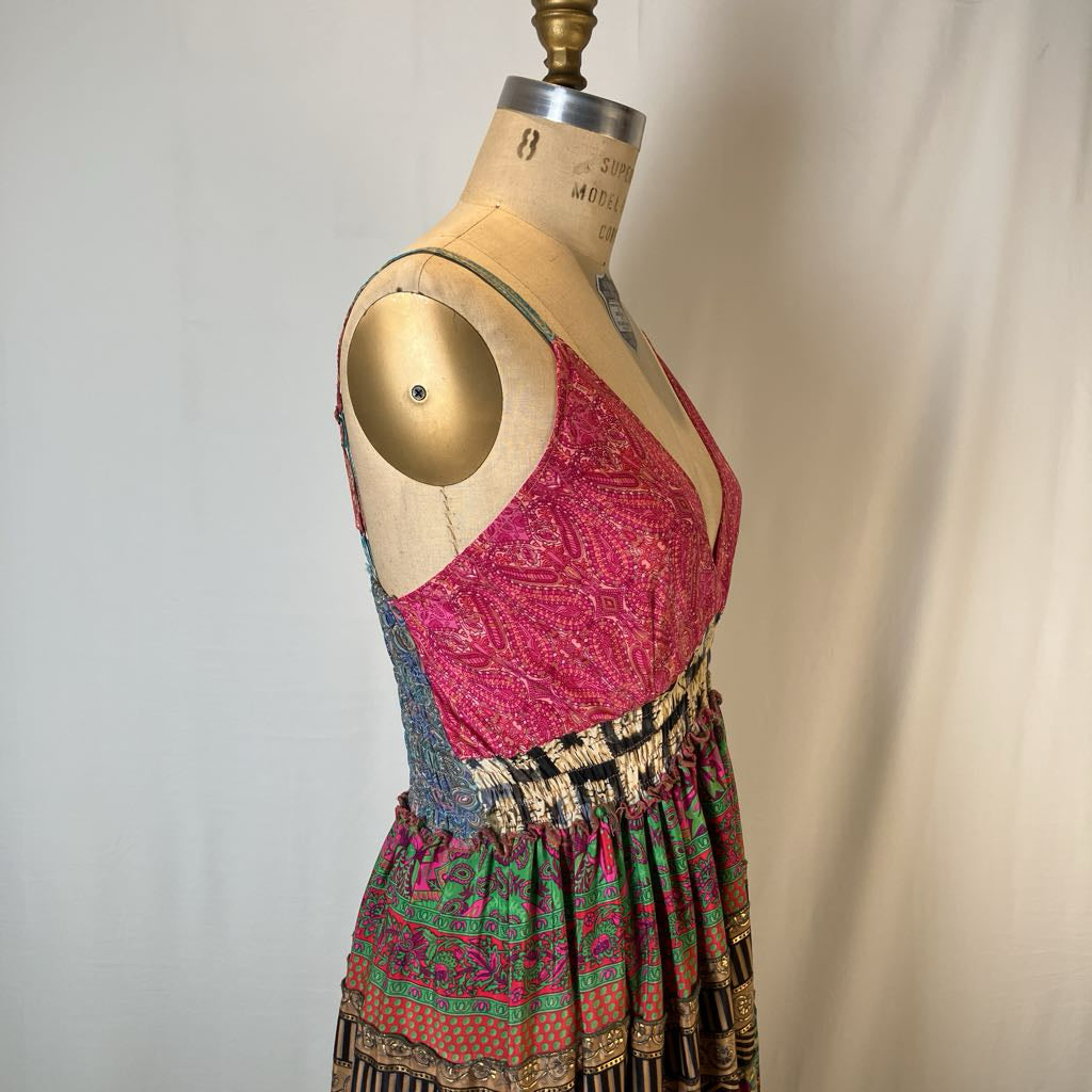 A vintage multicolor patterned dress displayed on a wooden dress form mannequin against a neutral off-white fabric backdrop.