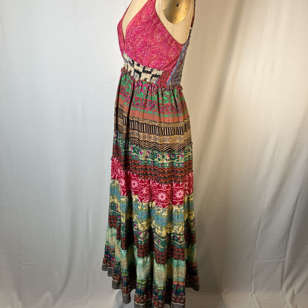 A sleeveless bohemian-style maxi dress displayed on a mannequin torso against a white fabric backdrop. The dress features a vibrant pink patterned bodice and a long, tiered skirt with intricate multicolor geometric and tribal patterns in pink, green, blue, brown, and beige.