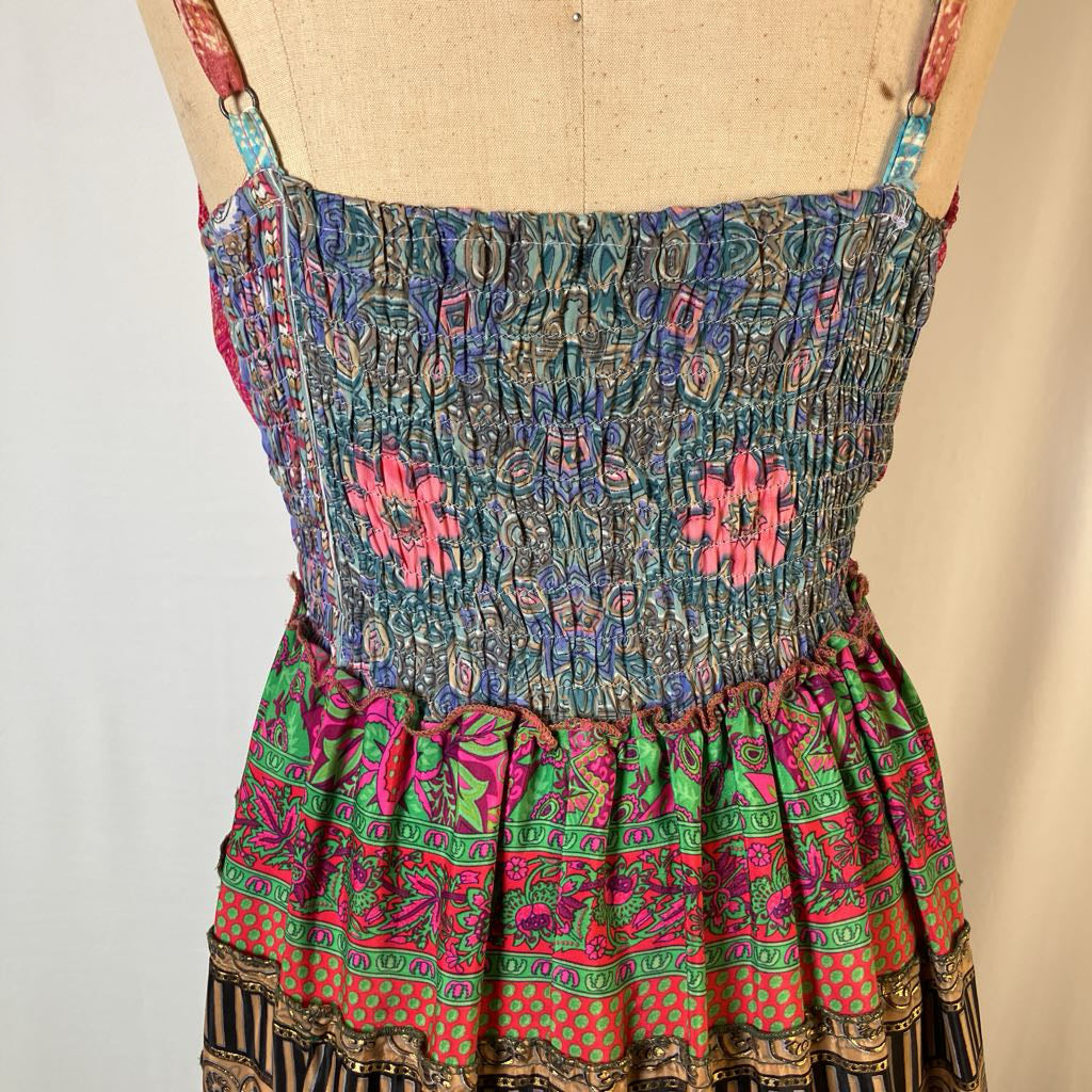 A sleeveless smocked bodice dress displayed on a tan dress form, featuring a multicolor patterned design with pink, green, blue, and orange tones.