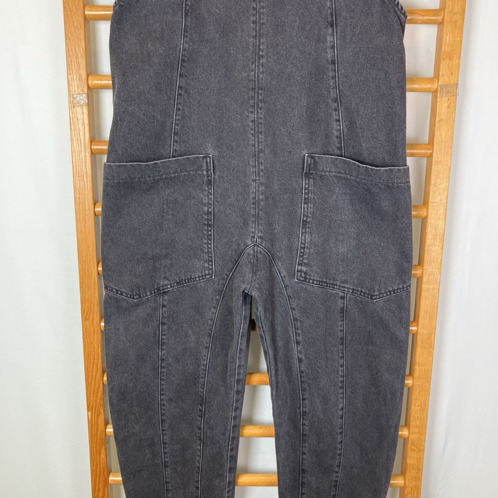 Dark gray washed denim overall with large front patch pockets, hanging on a wooden ladder against a white background.