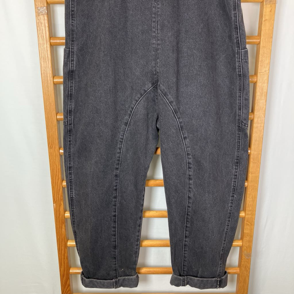 Dark gray washed denim pants with a unique curved leg design and rolled cuffs, displayed on a wooden hanger against a white background.