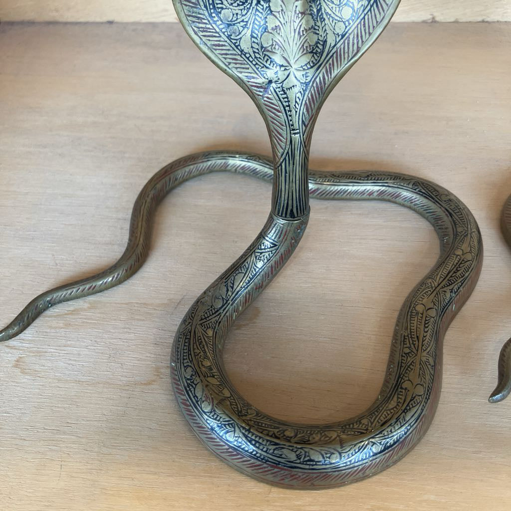 An ornate brass snake-shaped stand with intricate floral engravings, photographed on a light wood surface.