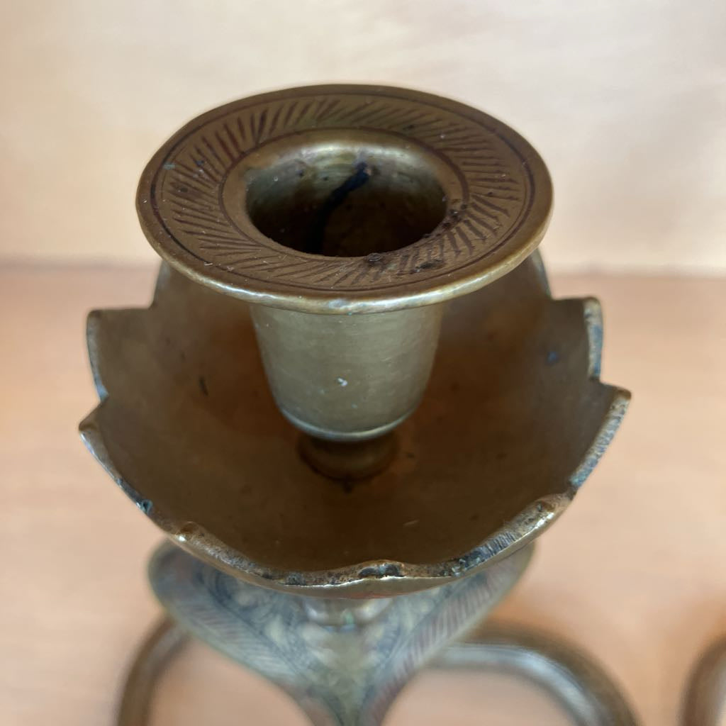 Close-up of a vintage brass candlestick holder showing the top cup and decorative rim, with a warm metallic finish and engraved details.