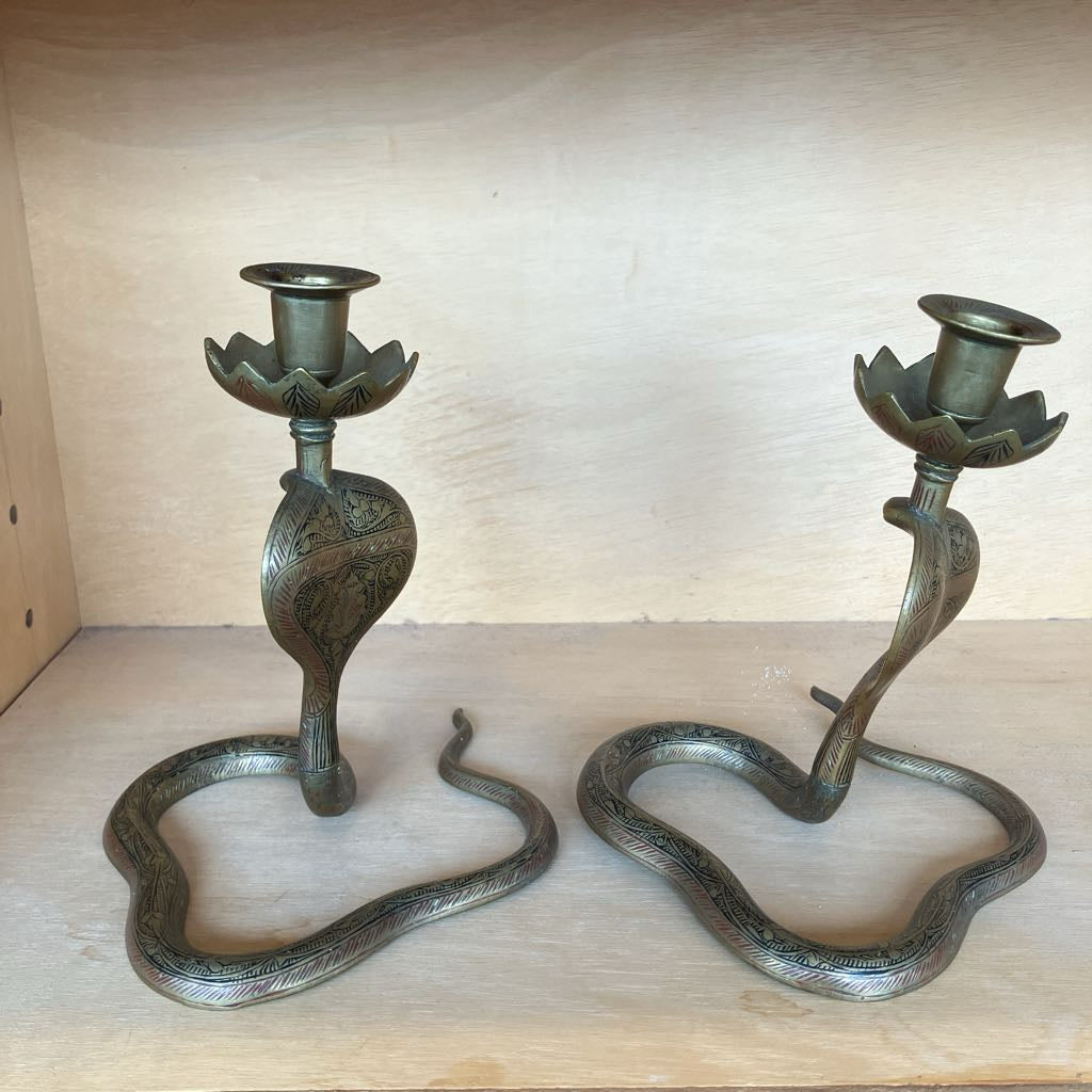 A pair of decorative snake-shaped candlesticks with lotus flower cup holders, shown on a light wood shelf.