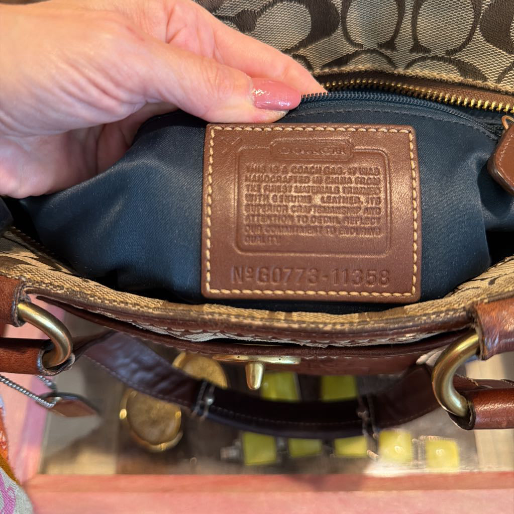 Close-up of a brown leather Coach interior label being held by a hand, showing the Coach logo and interior lining of a handbag.