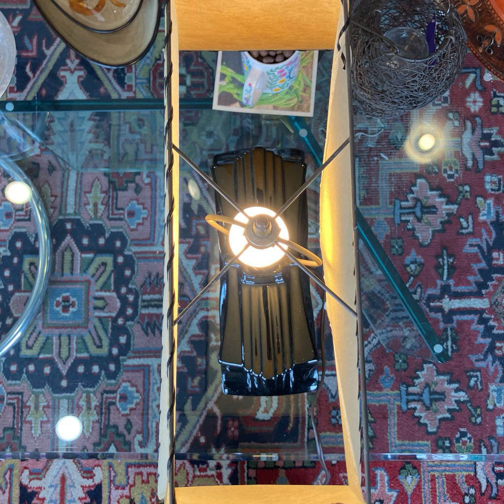 A vintage-style metal pendant light with a circular ring around the bulb, hanging from a wooden ceiling fixture over a patterned rug.