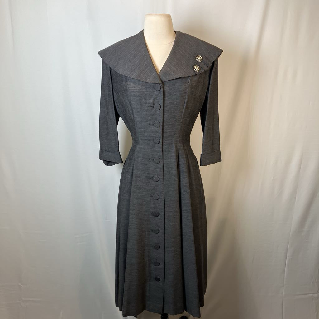 A gray three-quarter sleeve dress with a wide collar and front button closure, displayed on a mannequin against a light gray fabric backdrop.