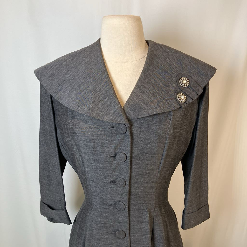 A gray textured vintage-style jacket with a wide collar and decorative buttons, displayed on a cream mannequin torso against a light neutral background.