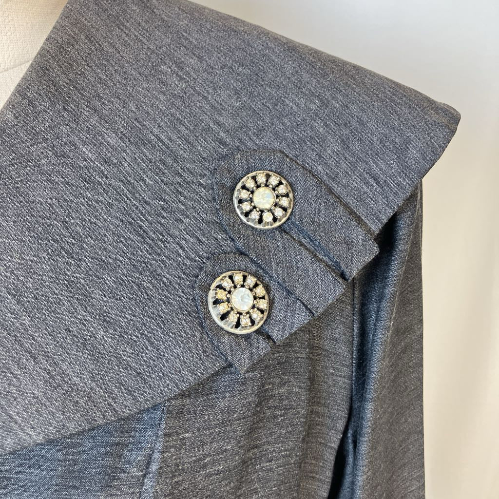 Close-up of a gray textured garment with two decorative round buttons featuring clear rhinestones on a light neutral background.