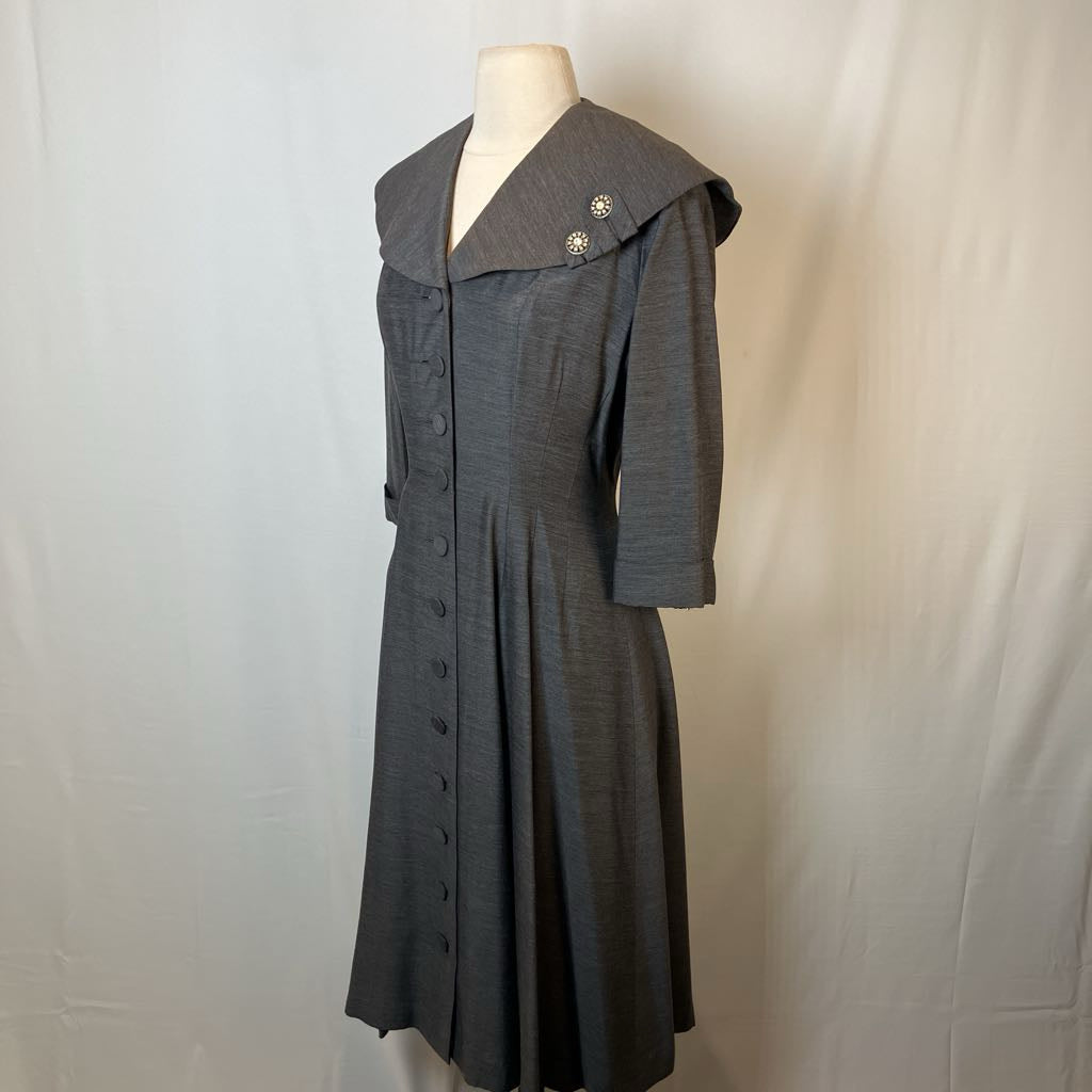 A dark gray textured dress with a wide collar and front buttons, displayed on a mannequin against a light gray fabric backdrop.