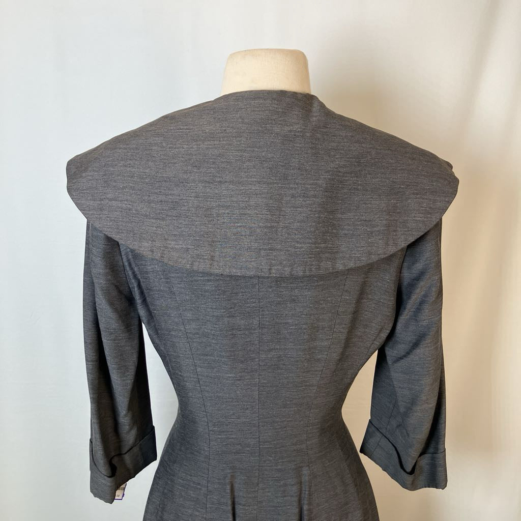 A gray three-quarter sleeve dress or jacket with a very wide, structured collar, shown from the back on a mannequin against a light off-white background.