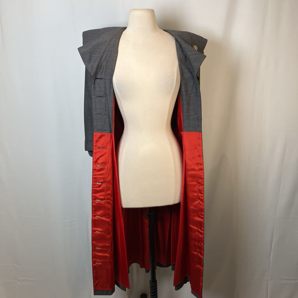 A long open-front coat or jacket displayed on a cream dress form mannequin against a light gray fabric backdrop. The garment has a dark gray outer section, a bright red satin-like inner lining, and a red lower panel with gray trim.