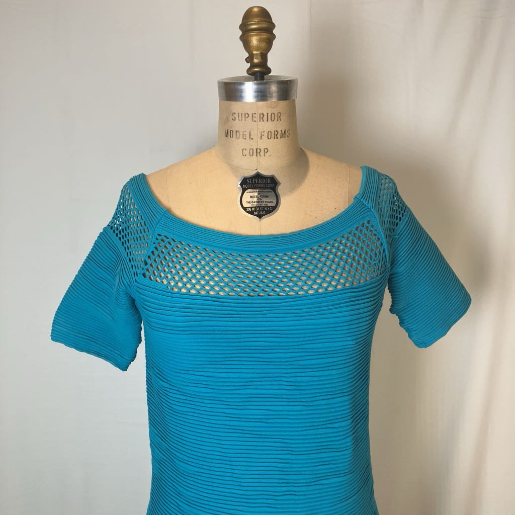 A turquoise blue short-sleeve knit top displayed on a vintage mannequin torso. The top features a wide scoop neckline with a semi-sheer, open-knit mesh panel across the chest and shoulders, and a fitted, horizontally ribbed body.