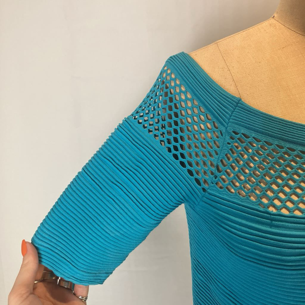 A turquoise blue ribbed knit top with a diamond-knit off-the-shoulder yoke, displayed on a tan dress form with a hand holding the sleeve.