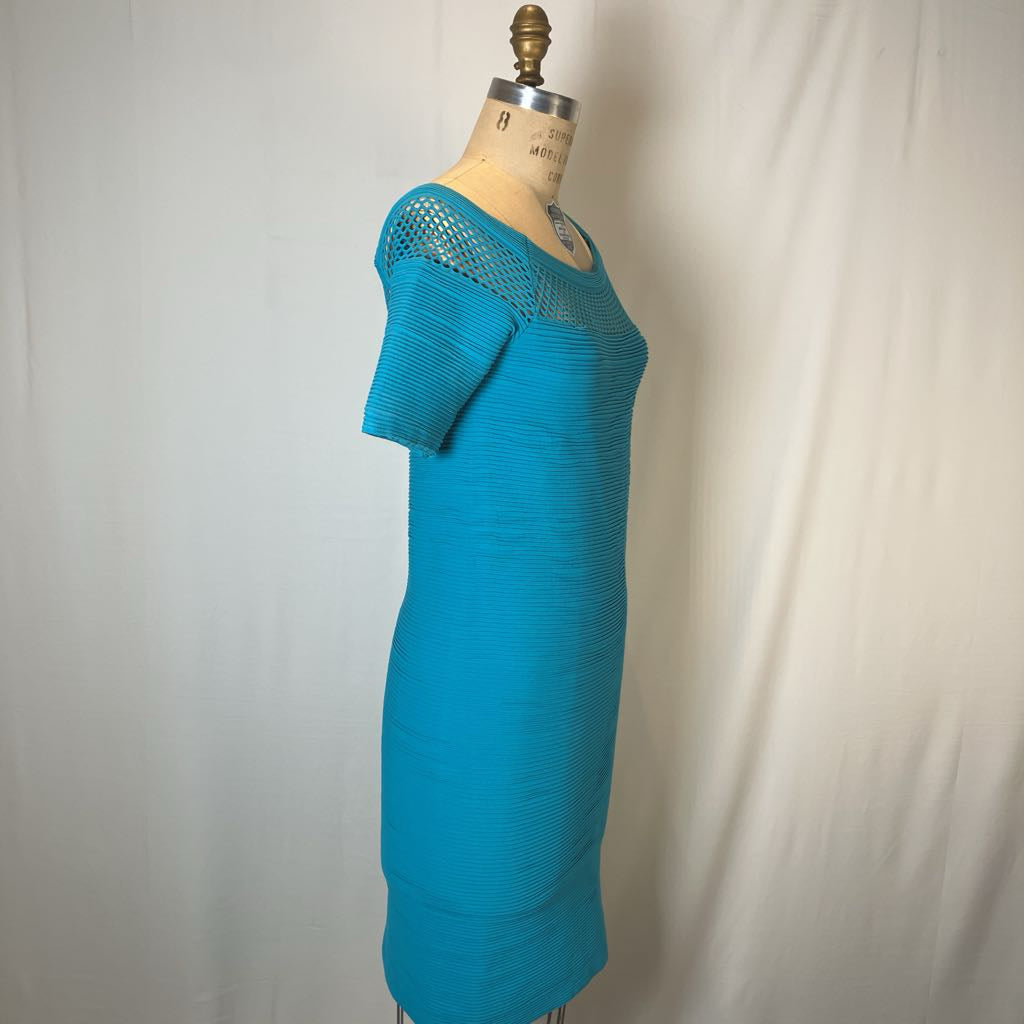 A turquoise blue short-sleeve knit dress displayed on a vintage wooden dress form mannequin against a white fabric backdrop.