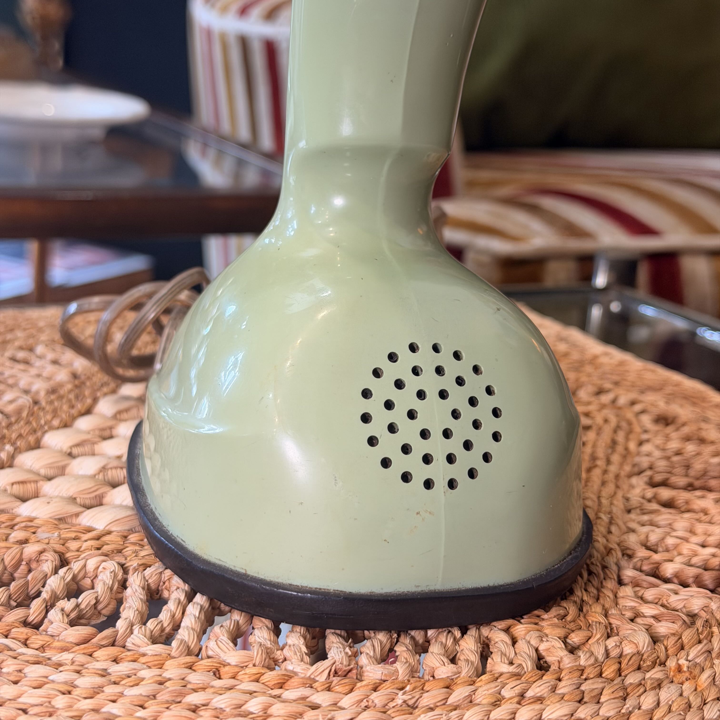 A vintage light green electric hair straightener with a circular vent pattern on the front, resting on a woven wicker placemat in a home setting.