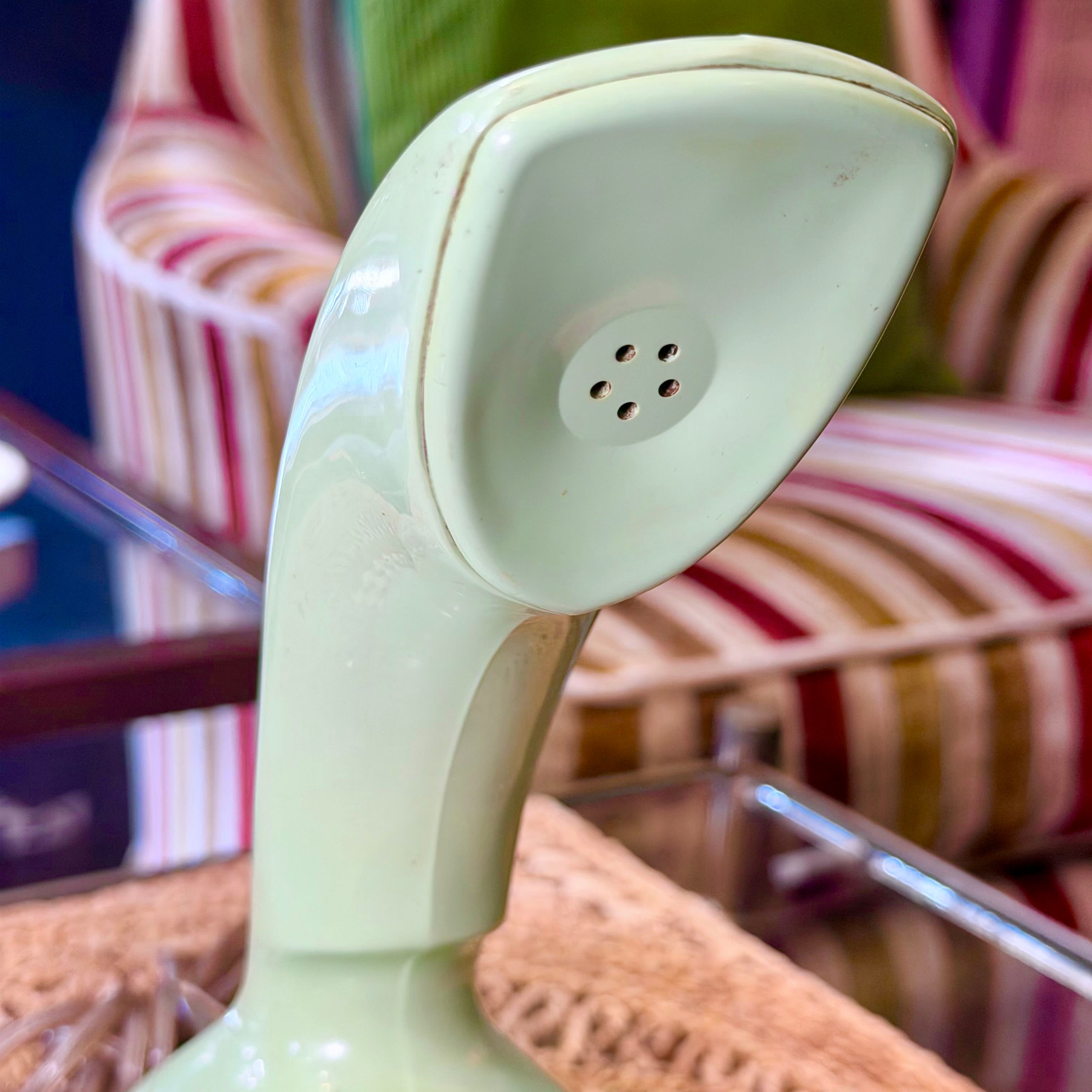 A vintage cream-colored ceramic telephone receiver handset shown in a close-up shot, resting on a textured surface with a striped armchair in the background.