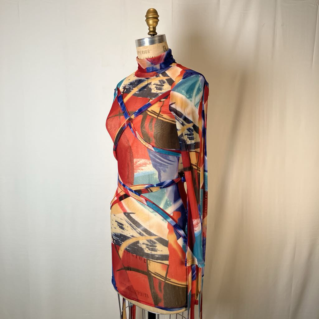 A multicolor abstract print wrap scarf displayed on a dress form mannequin against a light beige fabric backdrop.