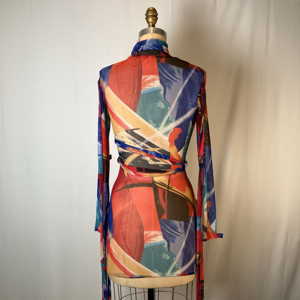 A long-sleeve wrap-style dress displayed on a dress form, featuring an abstract geometric print in red, blue, teal, beige, and black, set against a plain light background.