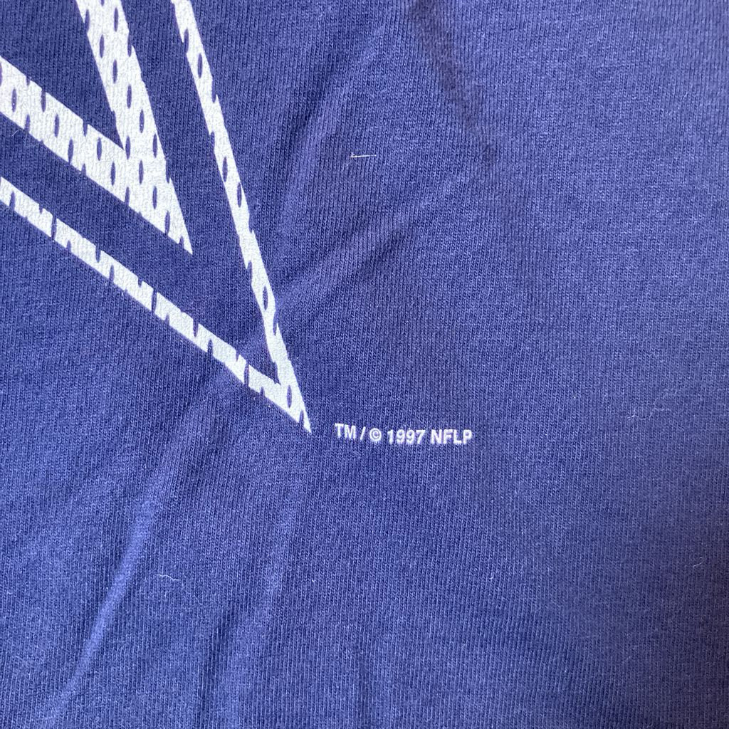 Close-up of a blue t-shirt fabric with a white geometric logo and small white text reading 'TM / © 1997 NFLP'.