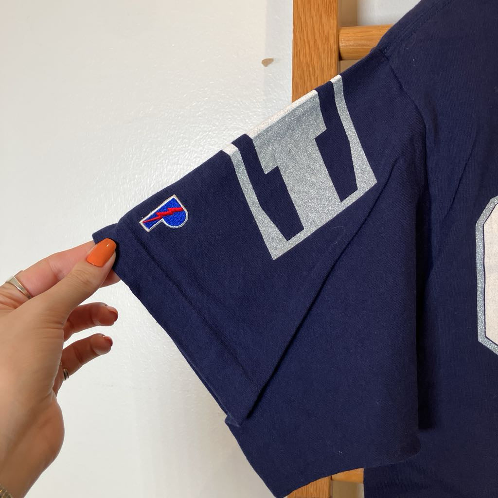 A navy blue vintage Buffalo Bills jersey sleeve is being held by a hand with orange nail polish. The sleeve features a large silver and white 'B' patch and a small embroidered Buffalo Bills logo.
