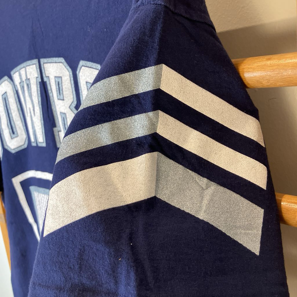 Close-up of a navy blue sweatshirt draped over a wooden chair, showing a large white and gray chevron stripe pattern on the sleeve and part of a white collegiate-style letter graphic on the chest.