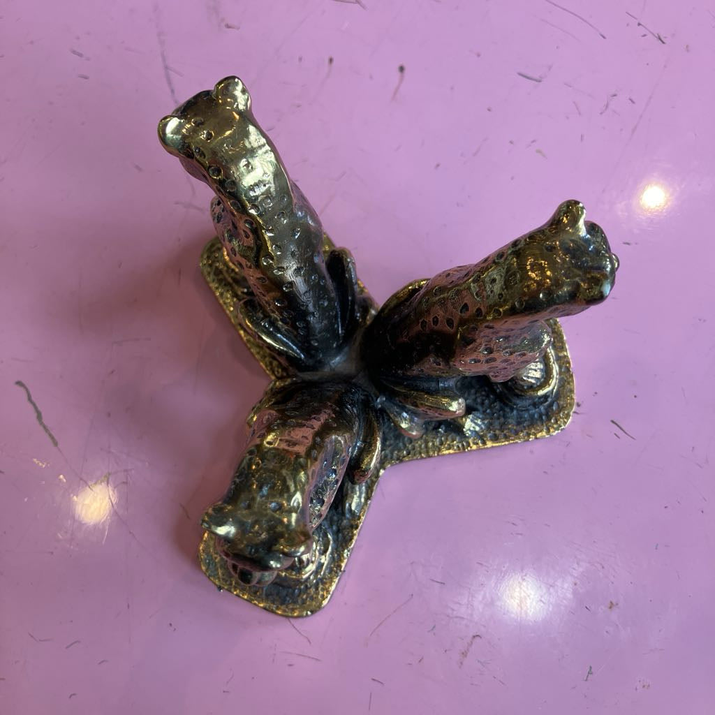A small metallic figurine shaped like three cheetahs clustered together, photographed on a pink surface with visible scratches and light reflections.