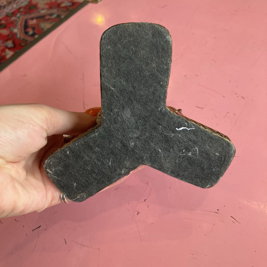 A hand holding a dark gray felt T-shaped block or pad against a pink background.