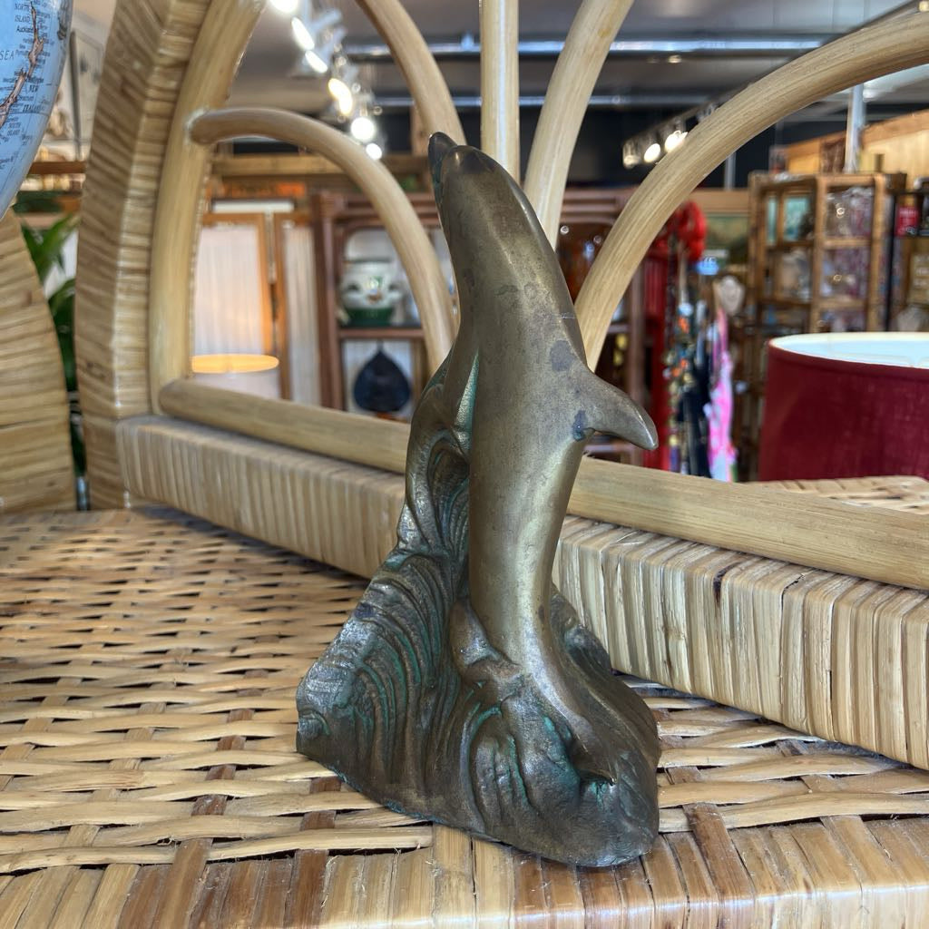 A bronze dolphin sculpture rising from stylized waves, displayed on a woven wicker surface inside a shop.