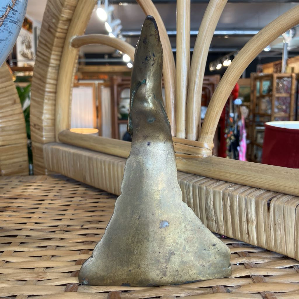 A vintage brass sculpture or decorative piece displayed on a woven rattan surface inside a shop.