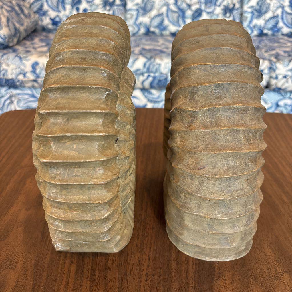 A pair of vintage wooden bookends shaped like coiled snakes, standing on a dark wood table with a blue and white patterned sofa in the background.