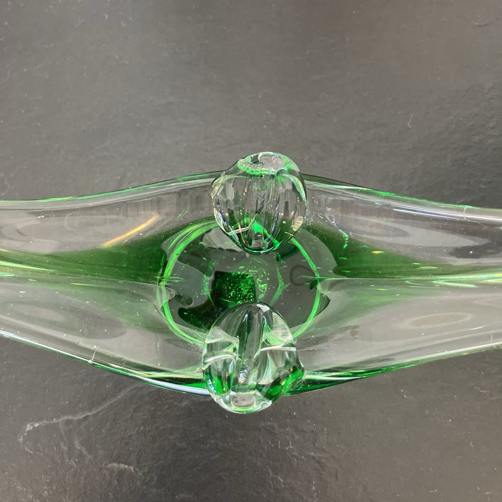 A close-up of a clear glass object with vibrant green internal coloring and two faceted green glass elements, set against a dark gray slate background.