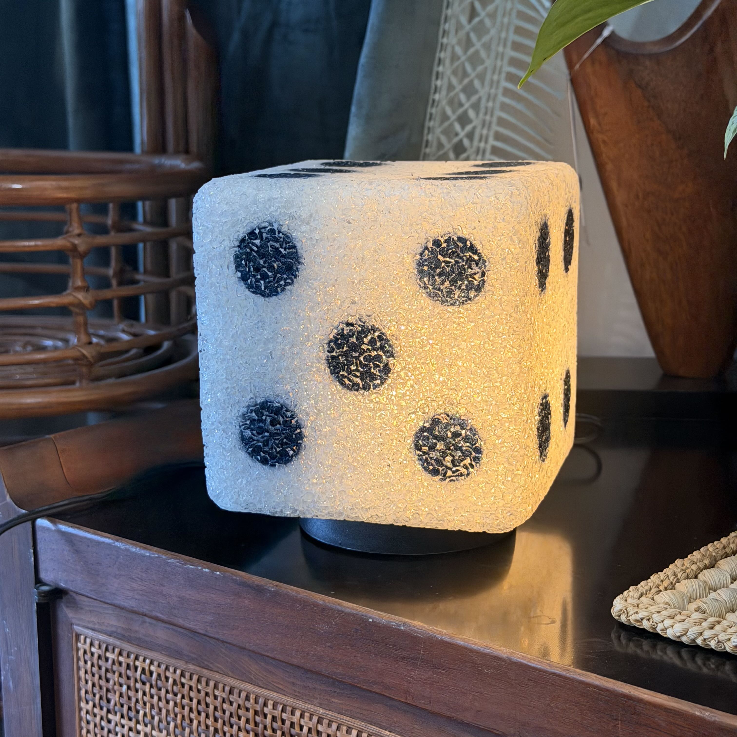 A cube-shaped decorative lamp or diffuser with a textured off-white surface and black speckled dots, sitting on a dark wooden table in a styled indoor setting.