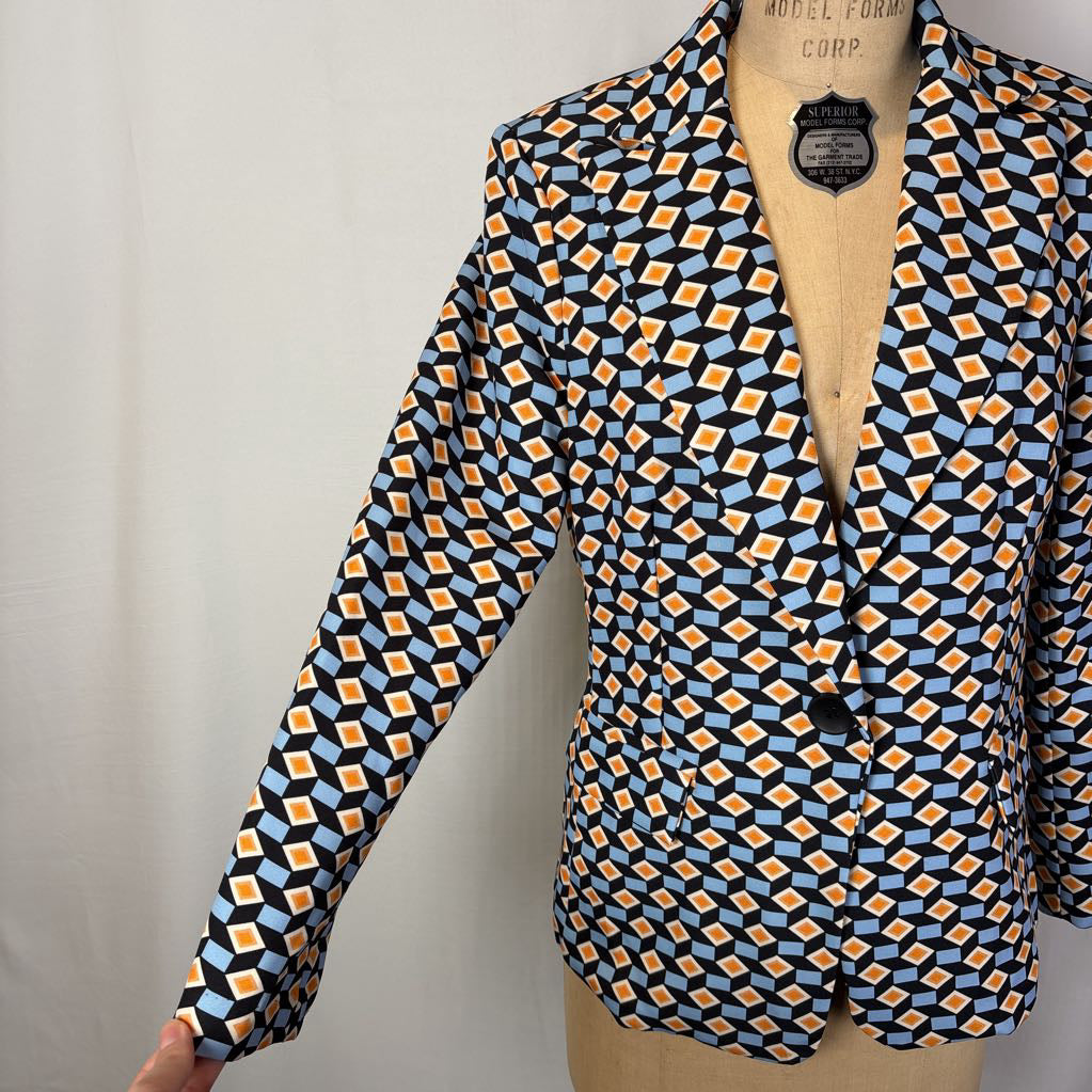 A blazer with a blue and orange geometric pattern on a mannequin against a white wall.