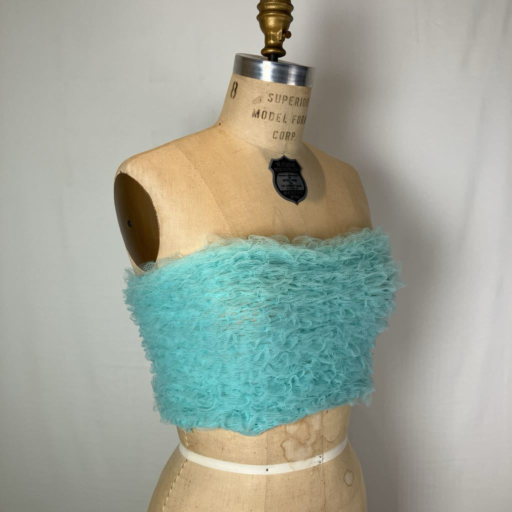 A turquoise fuzzy strapless tube top displayed on a vintage beige dress form mannequin against a white fabric backdrop.