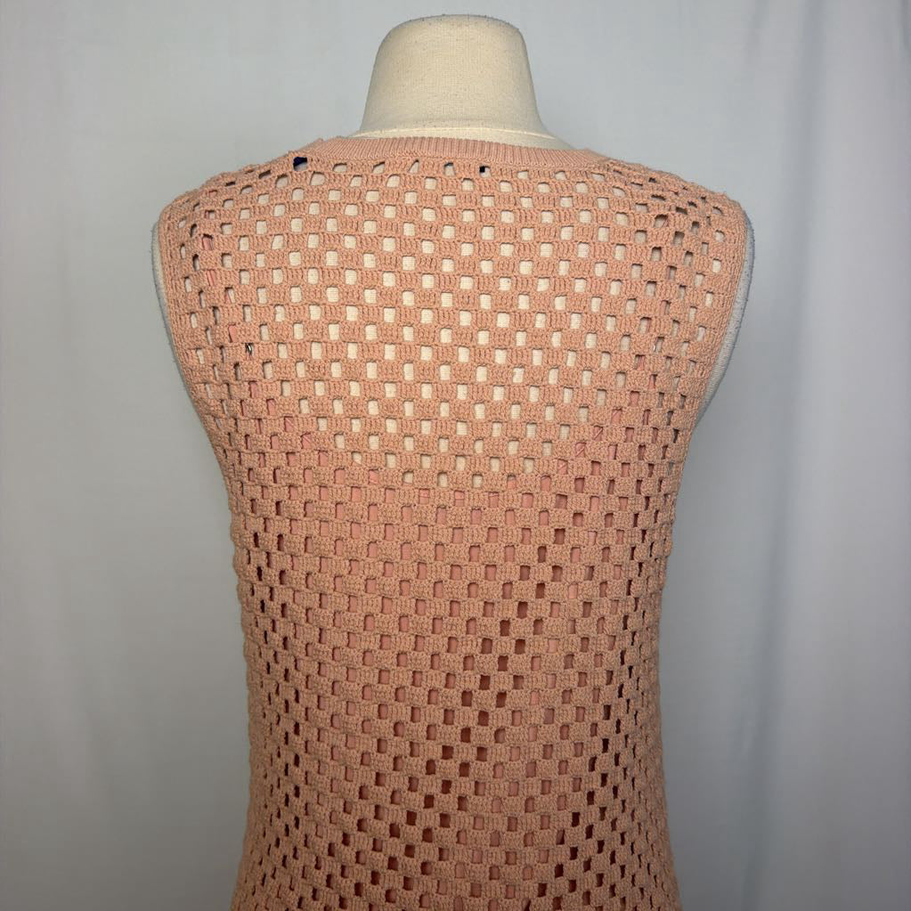 A sleeveless open-knit vest in a dusty peach-pink color, displayed on a cream-colored dress form mannequin against a light gray fabric backdrop.