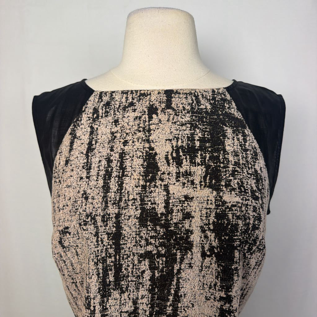 A sleeveless top displayed on a cream dress form mannequin, featuring a textured black and beige patterned front panel with solid black cap sleeves, set against a plain light gray background.
