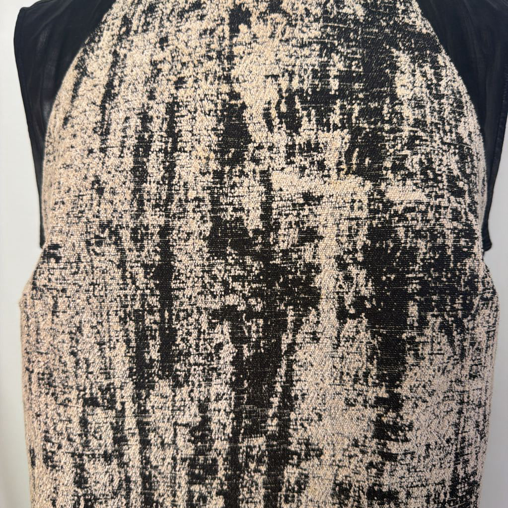 A close-up of a sleeveless top or dress featuring a distressed, textured pattern of black and warm beige/cream, with solid black raglan-style sleeves.