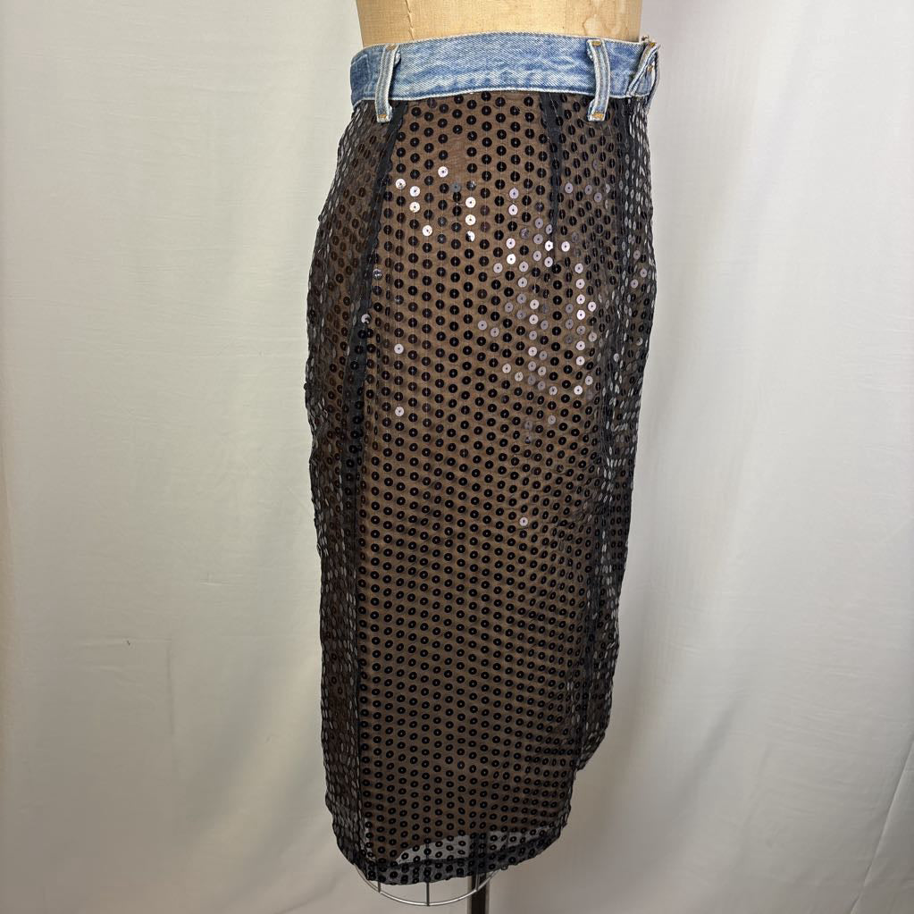 A black sequined mesh skirt with a denim waistband, displayed on a mannequin torso against a white fabric backdrop.
