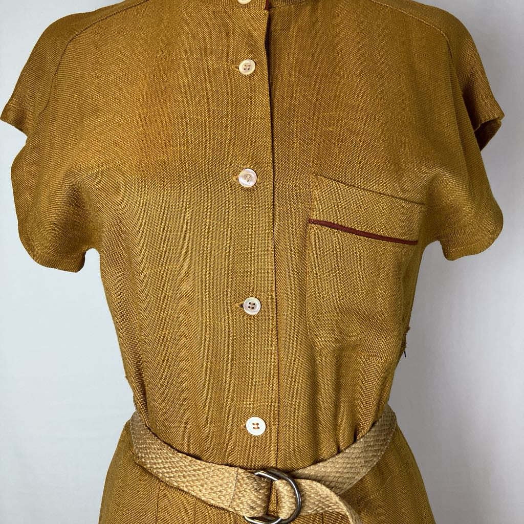 A mustard yellow linen shirt dress with short sleeves, a button-down front, a chest pocket with a thin red piping accent, and a matching woven belt with a metal ring buckle.