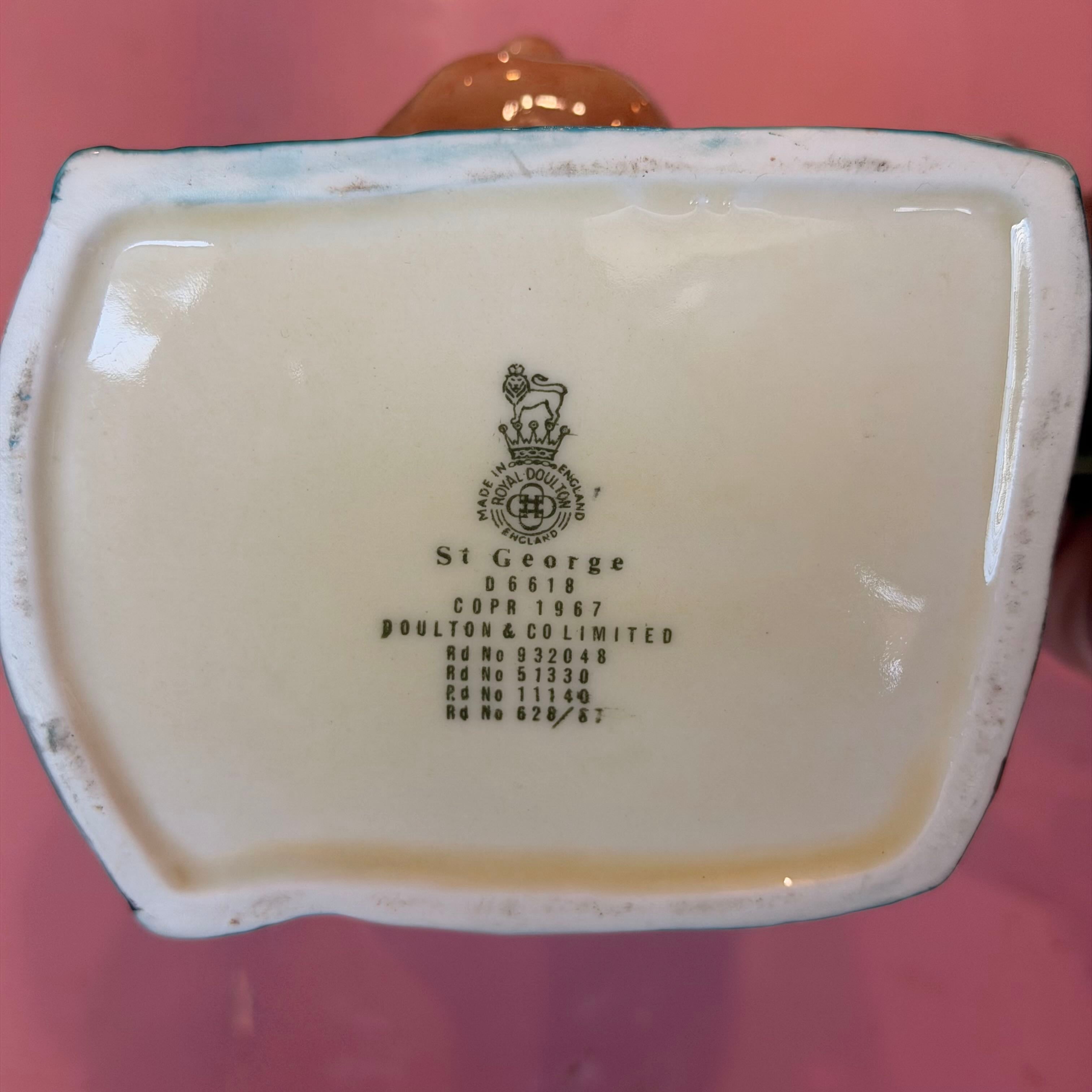 The underside of a ceramic St George mug, showing the printed manufacturer's mark and registration details for Poulton & Co Limited on a glossy cream glaze, set against a pink background.