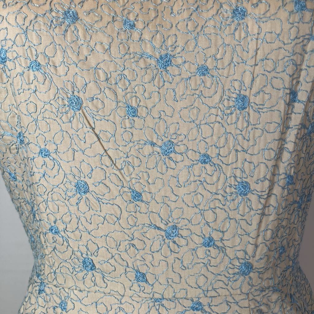Beige lace fabric with a blue floral pattern, shown on a dress form or mannequin torso.