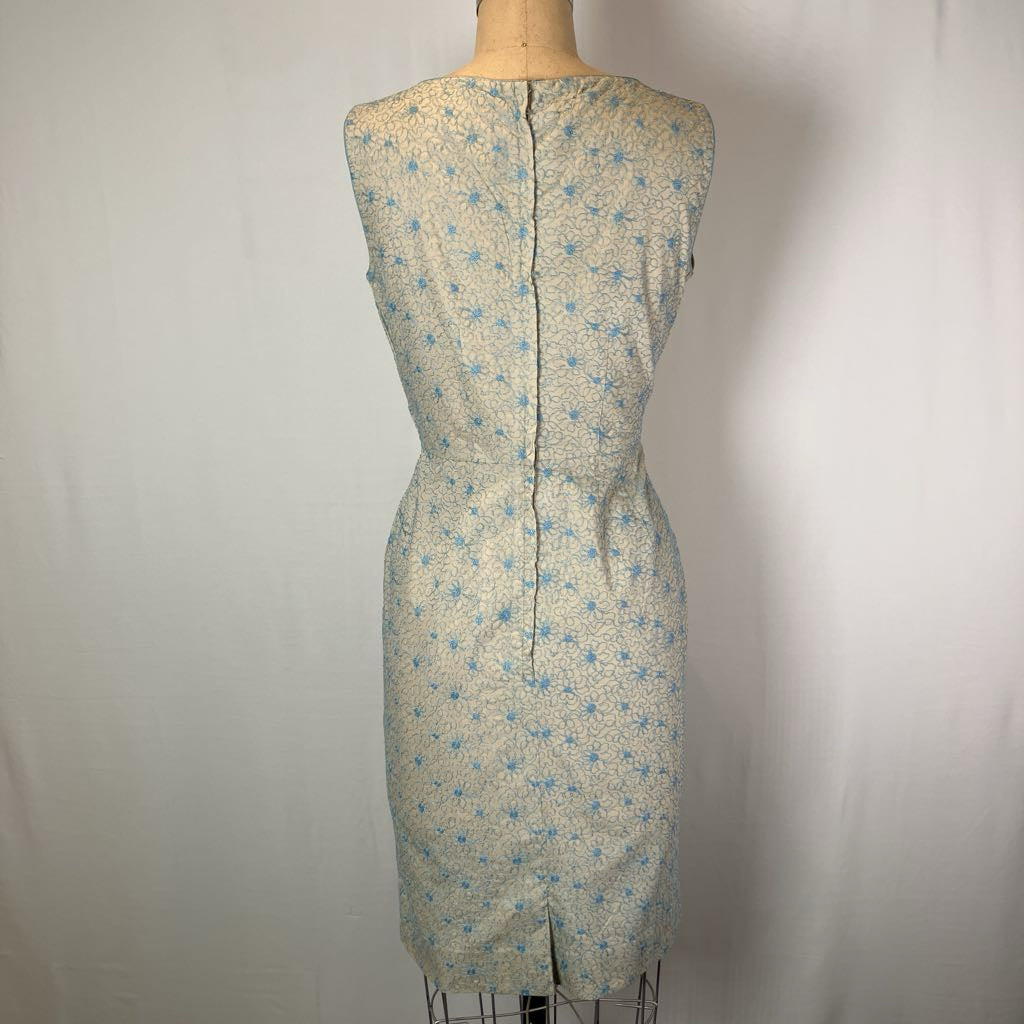 A sleeveless knee-length dress displayed on a mannequin, featuring a light beige or cream base with a small blue floral or star-like pattern and a central back zipper.