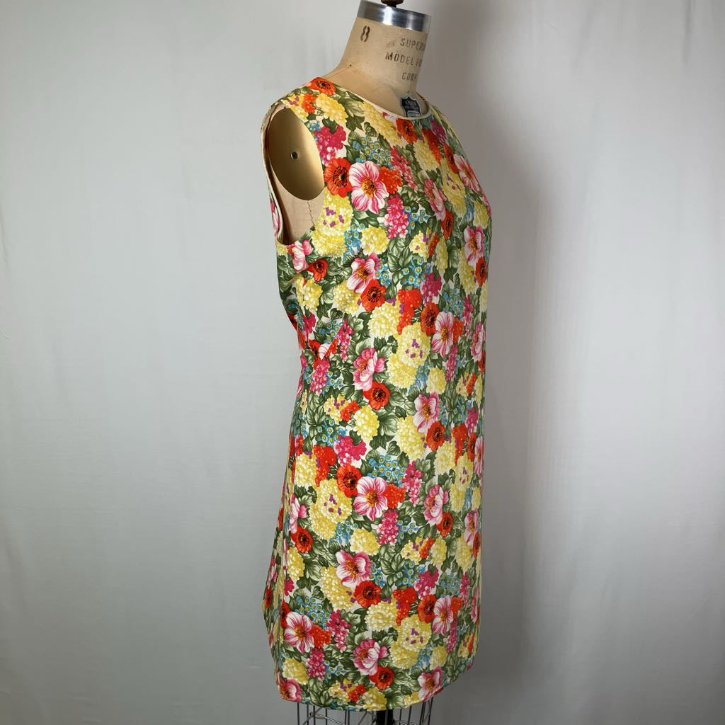 A sleeveless A-line dress with a vibrant multicolor floral print, displayed on a wooden dress form mannequin against a plain light gray background.