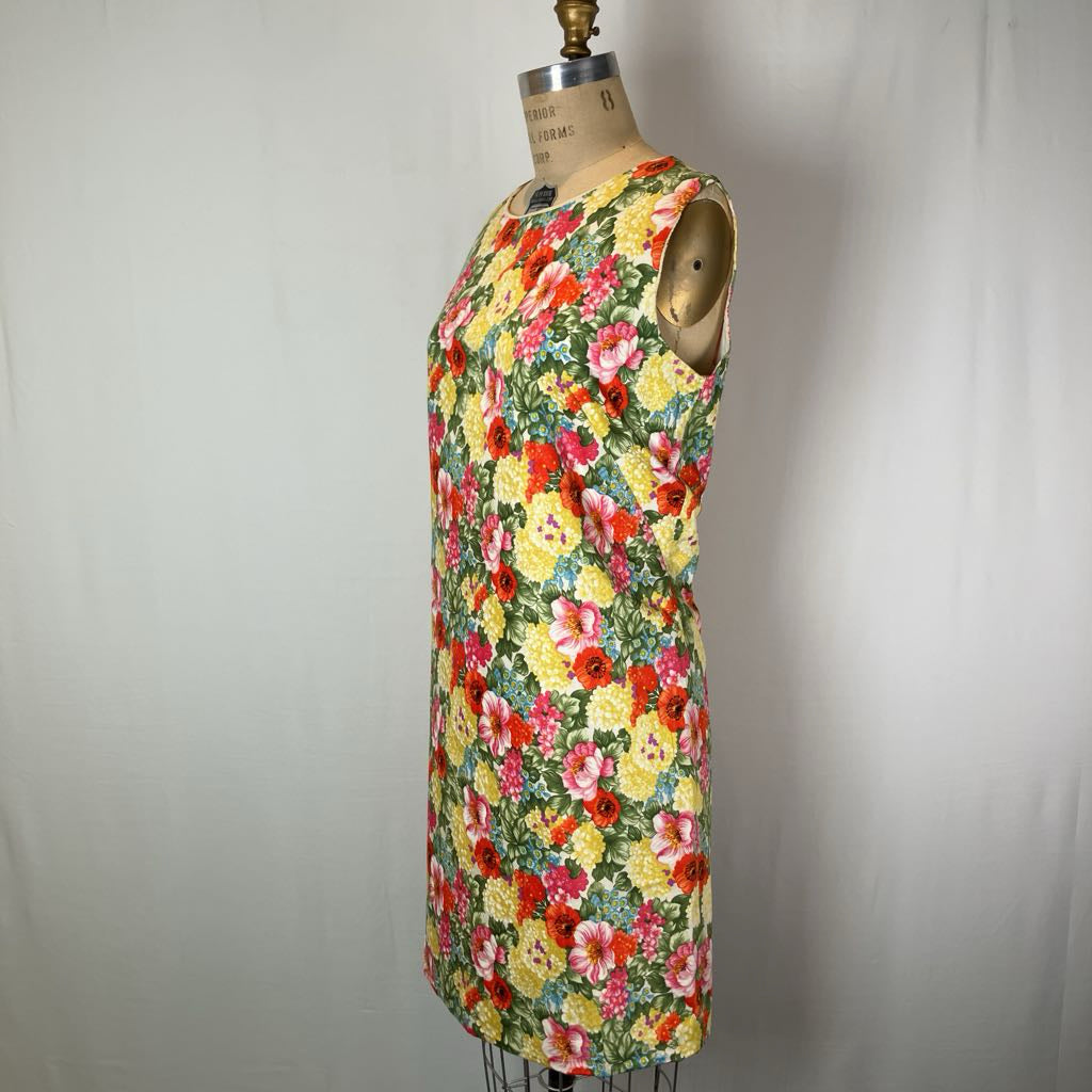 A sleeveless shift dress with a vibrant multicolor floral print, displayed on a vintage-style wooden dress form against a neutral light gray fabric backdrop.
