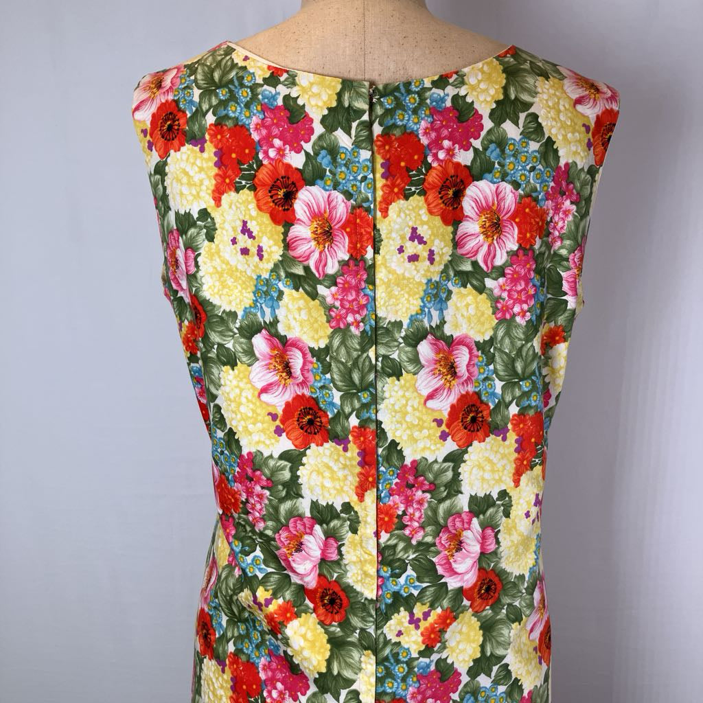 A sleeveless floral dress displayed on a mannequin torso, featuring a dense multicolor floral print with red, pink, yellow, and blue flowers on a green background.