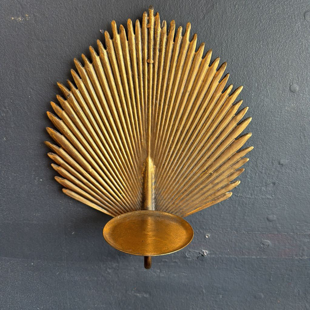 A mid-century modern brass wall sconce with a fan-shaped sunburst design and a circular tray base, mounted on a dark textured wall.