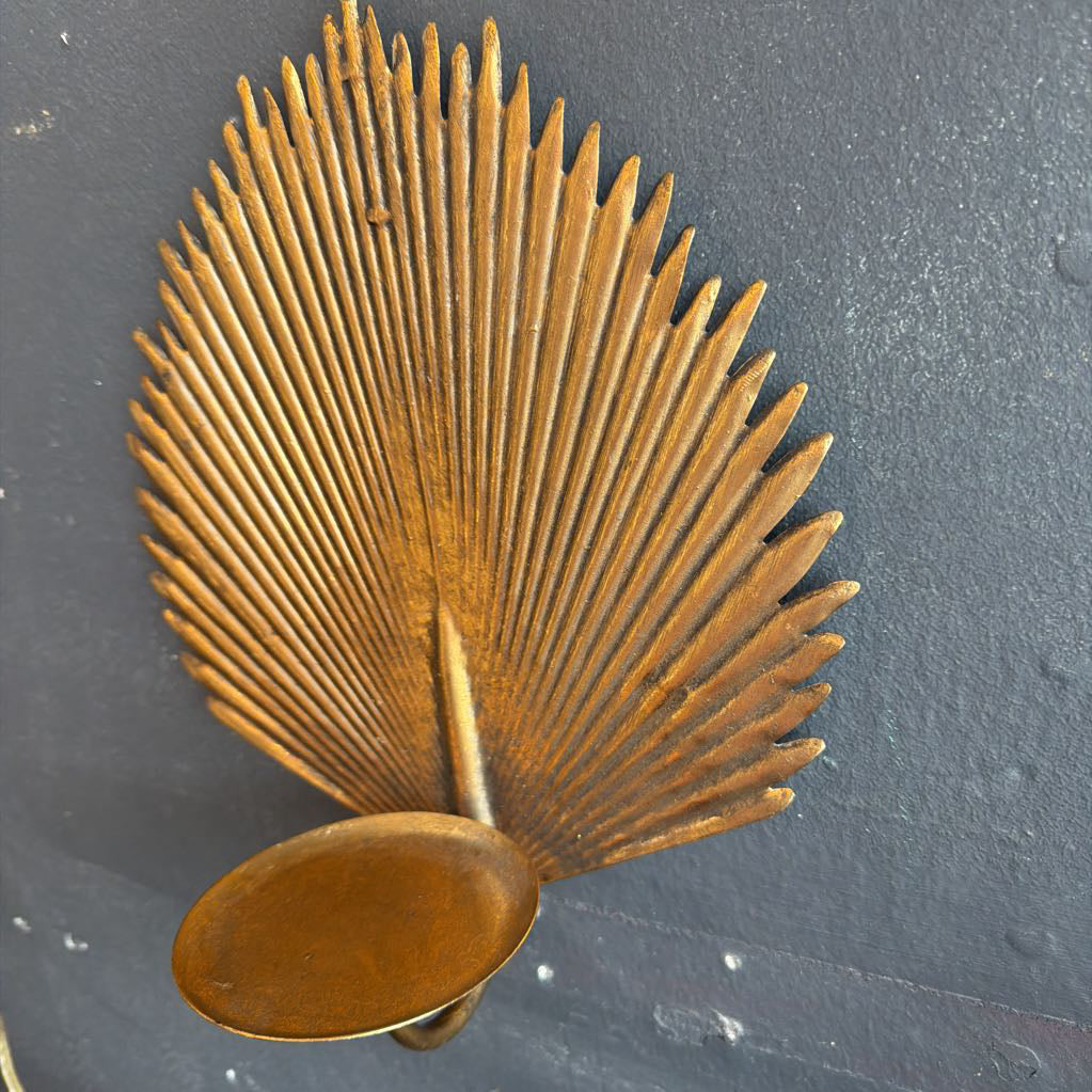 A vintage brass palm leaf wall sconce with a circular bowl-shaped shade, mounted against a dark textured wall.