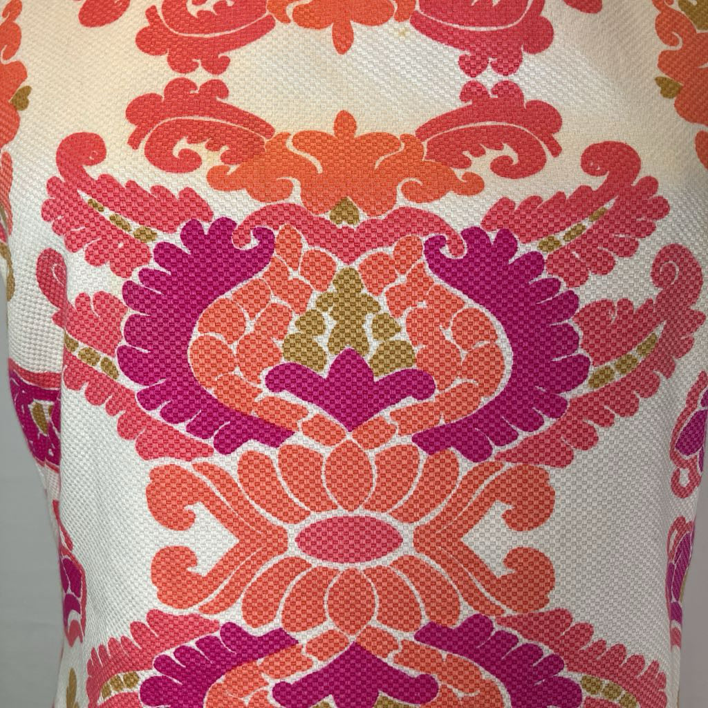 A close-up of a textured fabric featuring a vibrant, symmetrical damask pattern in shades of coral orange, magenta pink, and olive green on a cream-colored background.